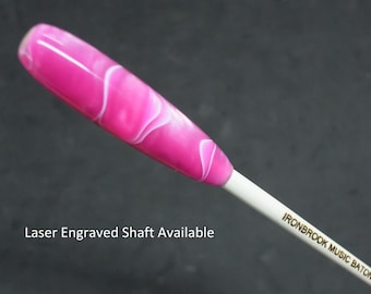 Puede incluir: Batuta de director con un mango veteado rosa y blanco vibrante. El eje blanco tiene el texto "IRONBROOK MUSIC BATONS" impreso. La imagen también incluye el texto "Laser Engraved Shaft Available".