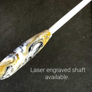 Pode incluir: Uma batuta marmoreada branca, preta e dourada com um eixo gravado a laser disponível.