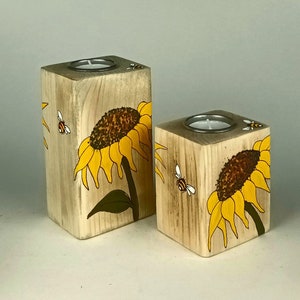 Puede incluir: Dos candelabros de madera con girasoles y abejas pintados a mano. Los candelabros en forma de bloques tienen una hendidura circular para una vela de t&eacute;. Los girasoles son amarillos y marrones, y las abejas son negras y blancas.