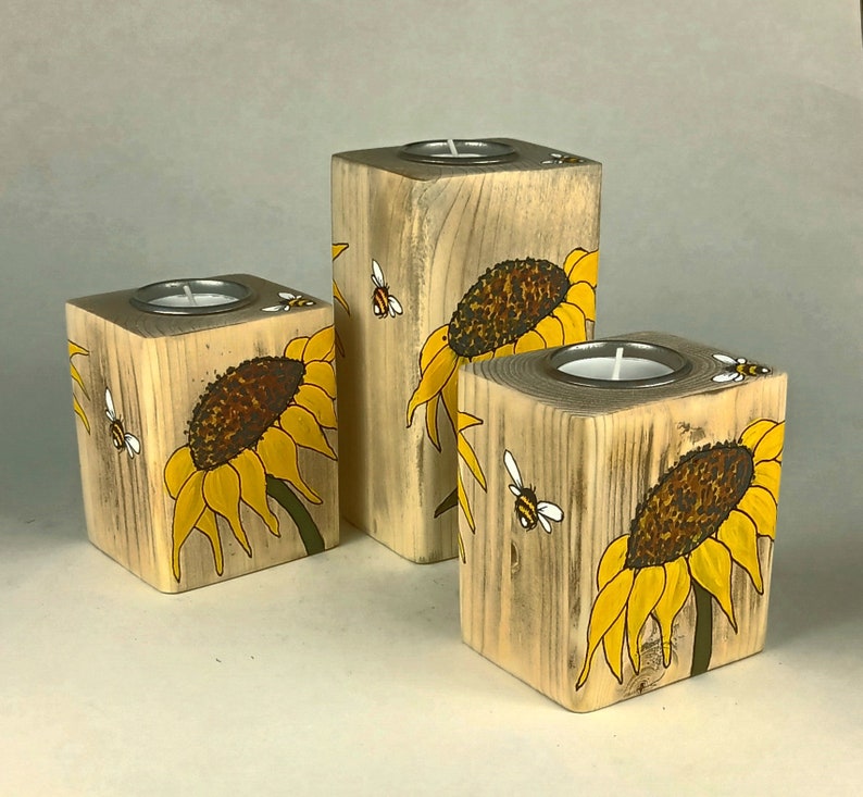 Puede incluir: Juego de tres candelabros de madera. Cada soporte cuadrado tiene una inserci&oacute;n de metal plateado para una vela de t&eacute;. Los bloques est&aacute;n pintados con girasoles amarillos y abejas.