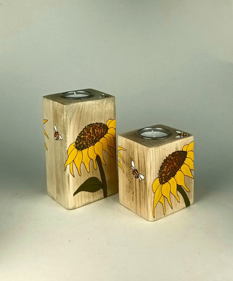 Puede incluir: Dos candelabros de madera con girasoles y abejas pintados a mano. Los candelabros en forma de bloques tienen una hendidura circular para una vela de t&eacute;. Los girasoles son amarillos y marrones, y las abejas son negras y blancas.