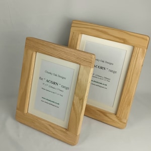 May include: Two light oak picture frames with off-white mounts. The frames are rectangular with a thick border. Text on the frames reads "Chunky Oak Designs" and "ACORN range". The frames are designed to hold 228mm x 177mm and 250mm x 200mm prints.