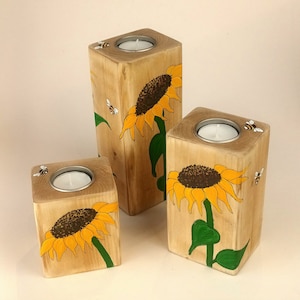 Puede incluir: Juego de tres candelabros de madera. Cada soporte es un bloque de madera natural con un dise&ntilde;o pintado de girasol y abeja. Los girasoles tienen p&eacute;talos amarillos y centros marrones. Cada soporte tiene una inserci&oacute;n de metal para una vela de t&eacute;.