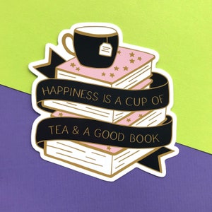May include: A sticker featuring a stack of books, a cup of tea, and the text "Happiness is a cup of tea & a good book". The books are pink and white with gold stars. The teacup is black with a tea bag.