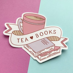 Könnte beinhalten: Eine rosa Teetasse mit einem Herzen und dem Text "TEA ♥ BOOKS" auf einem weißen Banner mit einem Stapel Bücher darunter.