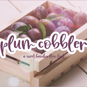 May include: A wooden crate filled with ripe purple plums. The crate is sitting on a white wooden surface. The text "plum-cobbler" is written in a purple handwritten font with a white outline.