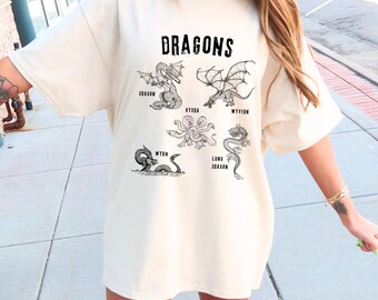 Peut inclure: Un t-shirt blanc surdimensionné avec un imprimé graphique noir de différents types de dragons. Le texte "DRAGONS" est imprimé en haut du graphique. Les noms de chaque dragon sont imprimés sous le graphique : "DRAGON", "WYVERN", "HYDRA", "WYRM", et "LONG DRAGON".