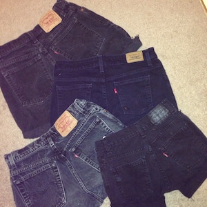 May include: Five pairs of dark blue denim jeans stacked on top of each other. The jeans are all different sizes and styles, but they are all made of a similar material.