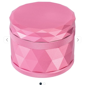 May include: Pink harlequin pattern grinder. This 4-part grinder features a geometric design with a textured, pink finish. The top and bottom are faceted, while the middle band has a dotted texture.