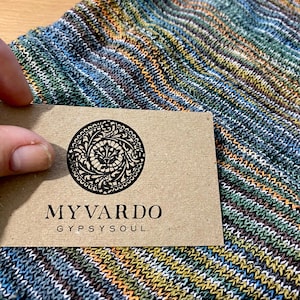 May include: A close-up of a striped fabric with a brown paper tag that says "MY VARDO GYPSY SOUL". The fabric is a mix of blue, green, orange, and white stripes.