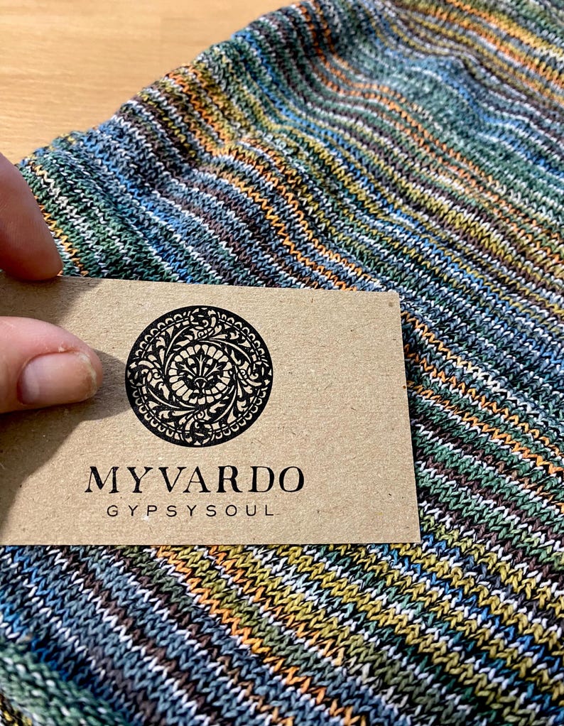 May include: A close-up of a striped fabric with a brown paper tag that says "MY VARDO GYPSY SOUL". The fabric is a mix of blue, green, orange, and white stripes.