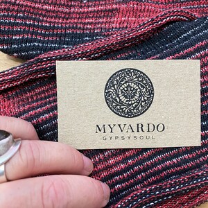 May include: A close-up of a red and black striped knit fabric with a business card that reads "My Vardo Gypsy Soul".
