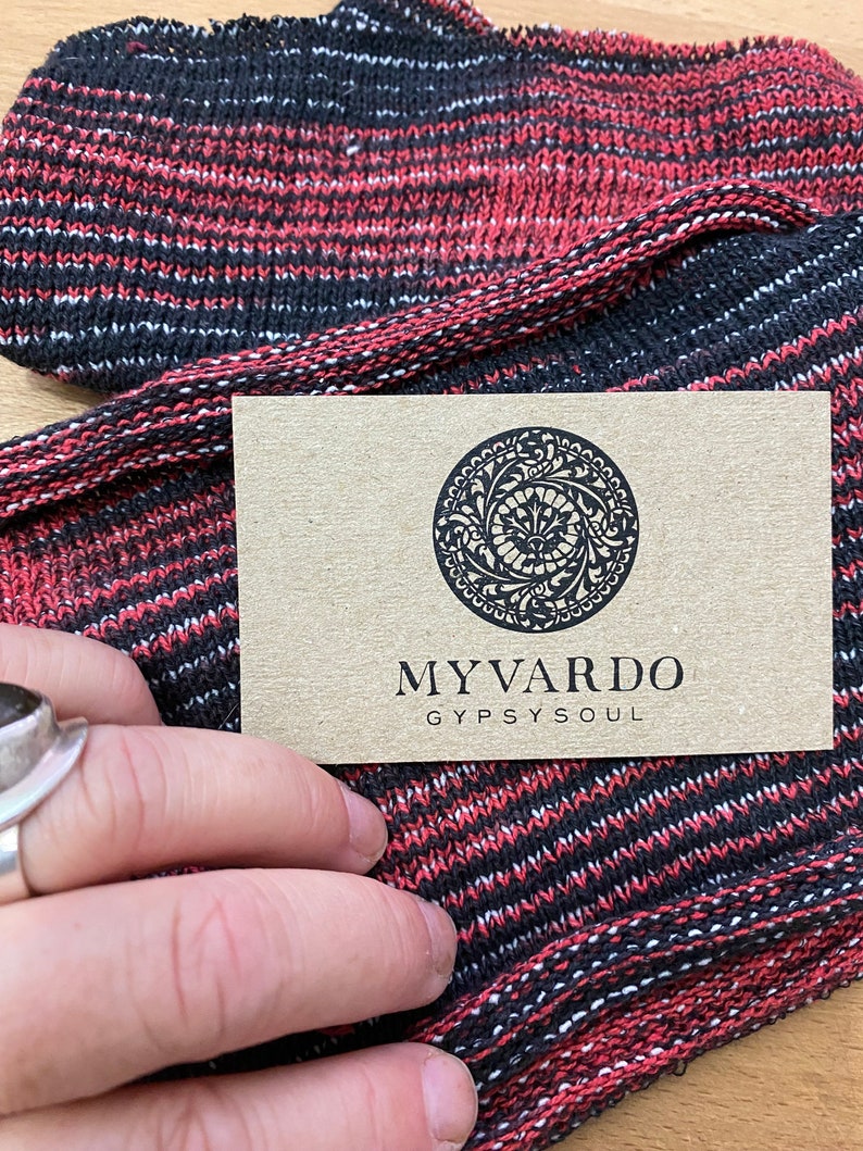 May include: A close-up of a red and black striped knit fabric with a business card that reads "My Vardo Gypsy Soul".