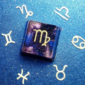 Könnte beinhalten: Ein Harz-Tastenkappen mit einem lila und blauen Galaxie-Design und einem goldenen Sternzeichen Jungfrau.