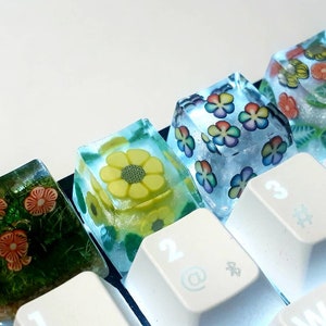 Puede incluir: Cinco teclas de resina de colores con diseños florales. Las teclas están dispuestas en un teclado blanco con los números 2, 3, 4 y 5 visibles.
