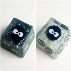 Könnte beinhalten: Zwei benutzerdefinierte Tastaturkappen mit einem schwarzen und weißen Unendlichkeits-Symbol-Design. Die Tastenkappen bestehen aus klarem Harz mit eingebettetem Glitzer. Die Tastenkappen sind quadratisch.