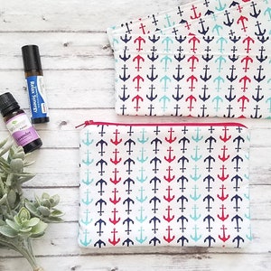May include: Two small bottles of essential oil with labels that read "Relax Synergy" and "Lavender". The bottles are sitting on a white wooden surface next to a small zippered pouch with a white background and a repeating pattern of red, blue, and turquoise anchors.