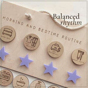 May include: A light-colored wooden board titled Morning and Bedtime Routine with the text Balanced rhythm. It features circular wooden tokens with black line icons for daily tasks and light purple plastic stars for tracking progress.