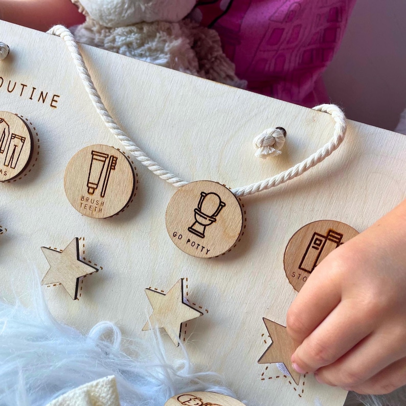 May include: Wooden daily routine board with circular icons for activities like brushing teeth and going potty. Includes star-shaped markers and a rope for hanging. The board is light-colored with engraved text and illustrations.