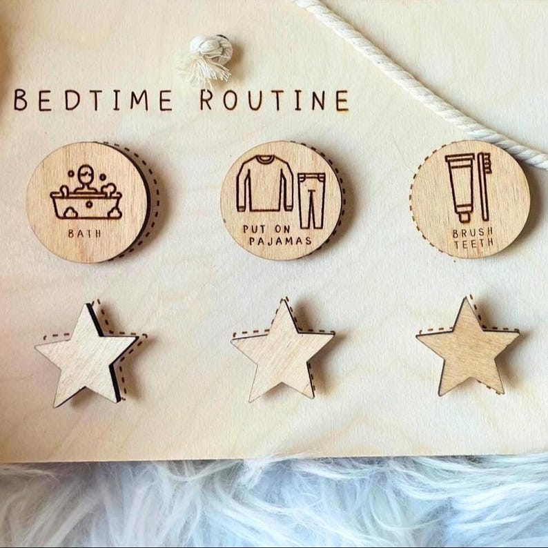 May include: Wooden bedtime routine chart with the words "BEDTIME ROUTINE" at the top. The chart includes three circular wooden icons with illustrations for bath, pajamas, and brushing teeth, along with three star-shaped wooden pieces.