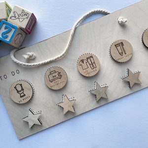 May include: Wooden 'To Do' board with a rope hanger, featuring engraved icons for daily tasks like 'Go Potty,' 'Eat Breakfast,' and 'Brush Teeth.' Includes wooden star-shaped markers and alphabet blocks.
