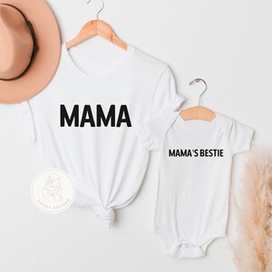 May include: White t-shirt with the word "MAMA" printed in black. A smaller white t-shirt with the text "MAMA'S BESTIE" printed in black.