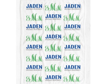May include: White baby blanket with a repeating pattern of green "SMM" monograms and the name "Jaden Michael McKinney" in blue text.