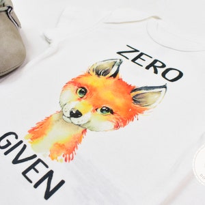 May include: White baby onesie with a watercolor illustration of a fox and the text "ZERO GIVEN".