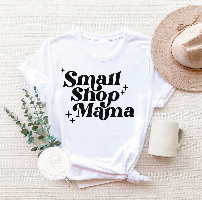 K&ouml;nnte beinhalten: Wei&szlig;es T-Shirt mit schwarzem Text, der "Small Shop Mama" in einem Retro-Schriftart-Stil lautet.