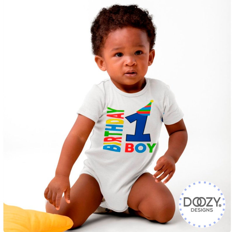 May include: A white baby onesie with a colorful "1st Birthday Boy" graphic. The number one is blue and has a party hat on top. The words "Birthday Boy" are in rainbow colors.