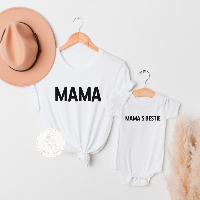 May include: White t-shirt with the word "MAMA" printed in black. A smaller white t-shirt with the text "MAMA'S BESTIE" printed in black.