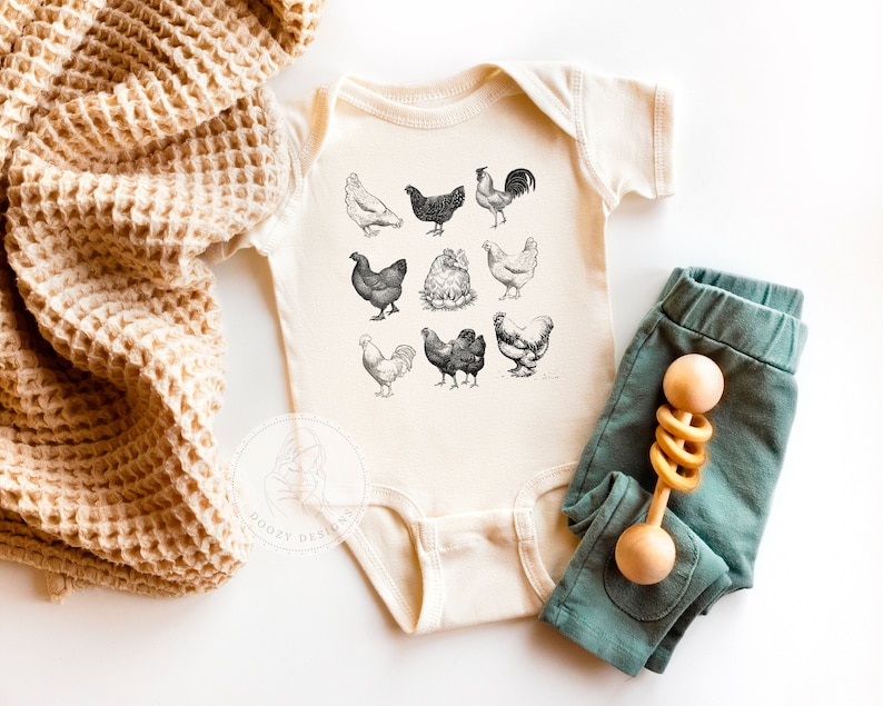 Short sleeve infant bodysuit in a neutral beige color. A graphic of vintage style chickens in black and white printed on the front.
