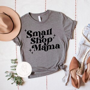 K&ouml;nnte beinhalten: Graues T-Shirt mit dem Text "Small Shop Mama" in schwarzen Retro-Lettern.
