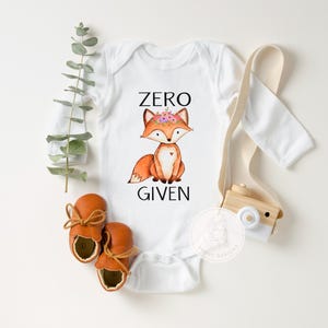 Op de afbeelding: Witte romper met lange mouwen met een vos die een bloemenkrans draagt en de tekst "ZERO GIVEN".