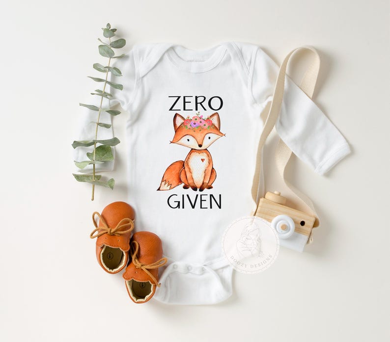 Op de afbeelding: Witte romper met lange mouwen met een vos die een bloemenkrans draagt en de tekst "ZERO GIVEN".