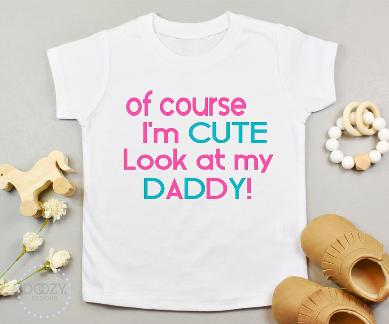 May include: White baby onesie with pink and teal text that reads "of course I'm CUTE Look at my DADDY!"