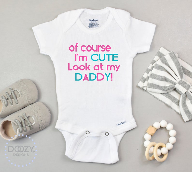 May include: White baby onesie with the text "of course I'm CUTE Look at my DADDY!" in pink and teal lettering.