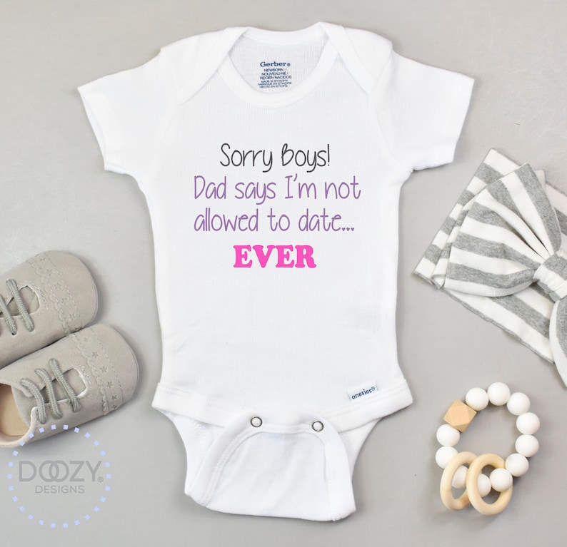 Pode incluir: Macac&atilde;o branco para beb&ecirc; com o texto "Sorry boys! Dad says I'm not allowed to date... EVER" em letras roxas e rosa.