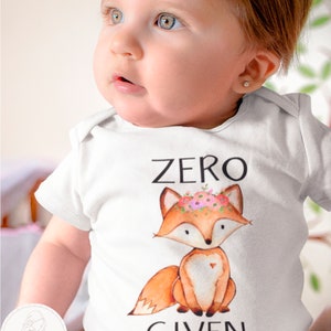 Op de afbeelding: Witte baby romper met een vos die een bloemenkrans draagt en de tekst "ZERO GIVEN".