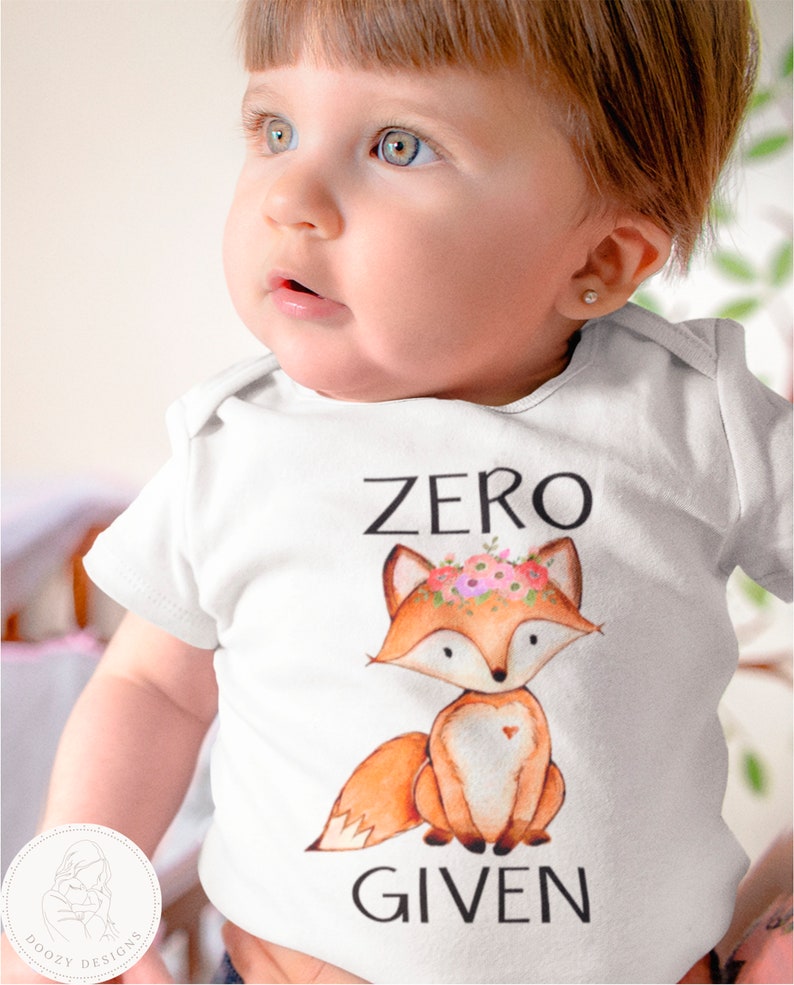 Op de afbeelding: Witte baby romper met een vos die een bloemenkrans draagt en de tekst "ZERO GIVEN".