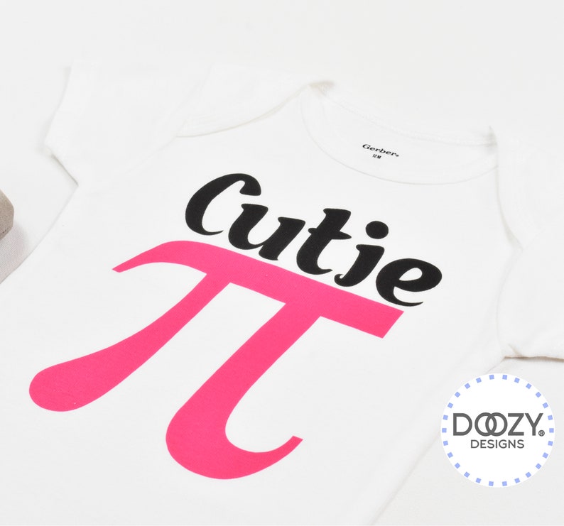 Pu&ograve; includere: Un body bianco per neonato con un simbolo pi rosa e la parola "cutie" in testo nero. Il body ha un piccolo logo nell'angolo in basso a destra che dice "Doozy Designs".