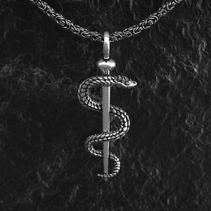 May include: A silver necklace with a pendant featuring a snake wrapped around a staff, a symbol of medicine.