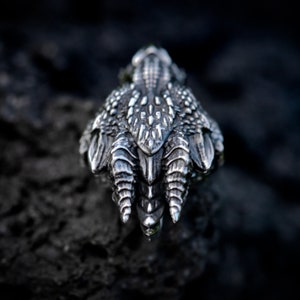 May include: A silver dragon claw ring with detailed scales and sharp claws. The ring is set against a dark background.