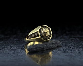 May include: A gold-toned ring featuring an octagonal face with a detailed wolf head relief. The sides of the band display a textured, cross-hatched pattern. The ring is crafted with a polished finish and sharp, defined geometric edges.