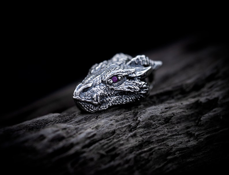 May include: A silver dragon head ring with a purple gemstone eye.