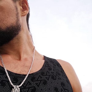 May include: A silver chain necklace with a dragon head pendant. The necklace is worn by a person wearing a black tank top with a geometric pattern.