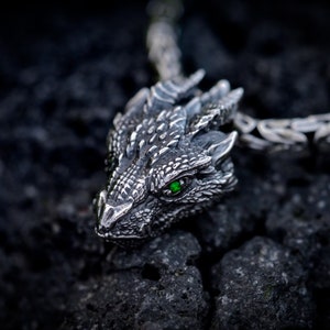 May include: A silver dragon pendant with a green gemstone eye. The pendant is attached to a silver chain.