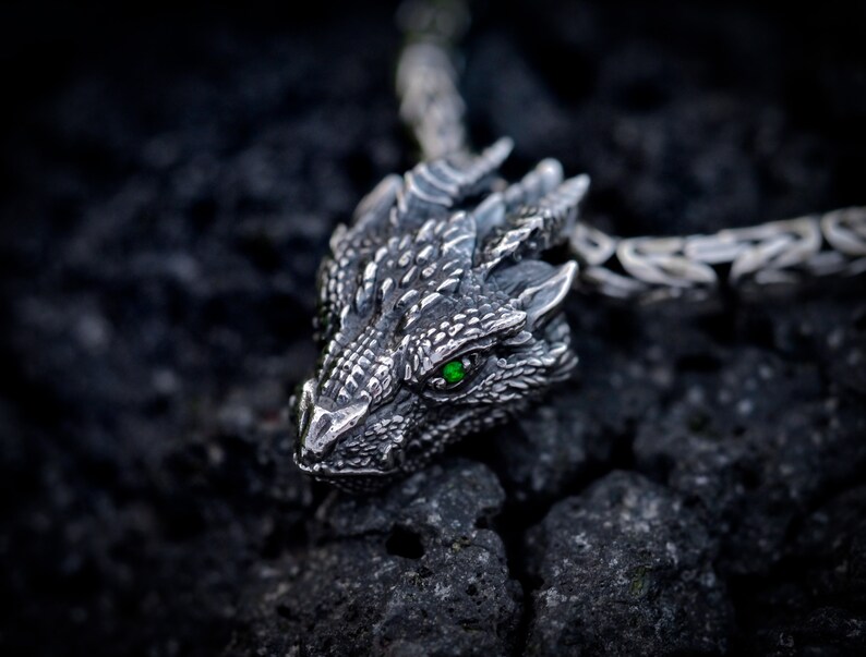 May include: A silver dragon pendant with a green gemstone eye. The pendant is attached to a silver chain.