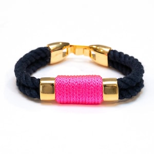 May include: A black rope bracelet with gold accents and a bright pink rope accent.