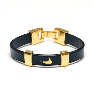 May include: A navy blue leather bracelet with gold accents and a gold outline of an island.
